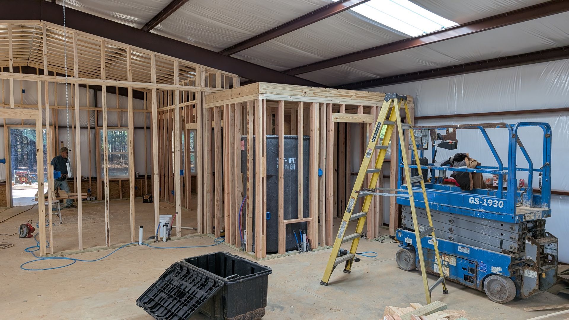 Interior construction with wooden framing and a lift; a person works.