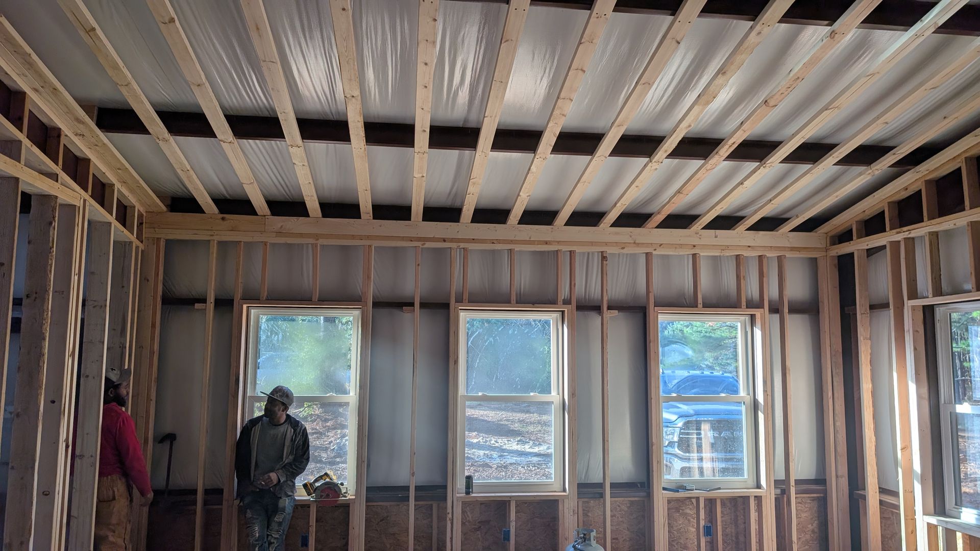Interior view of a building under construction, showing wooden framing, windows, and exposed ceiling beams. A person is visible.
