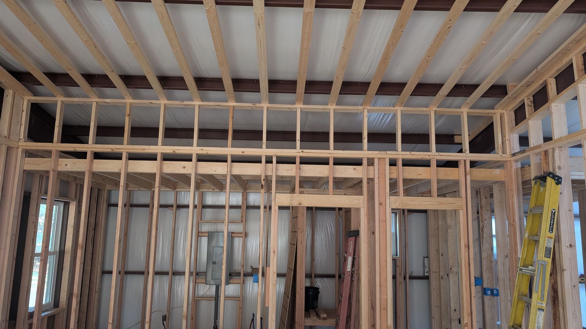 Interior view of a building under construction, showing wooden framing for walls and ceiling, with open doorways.