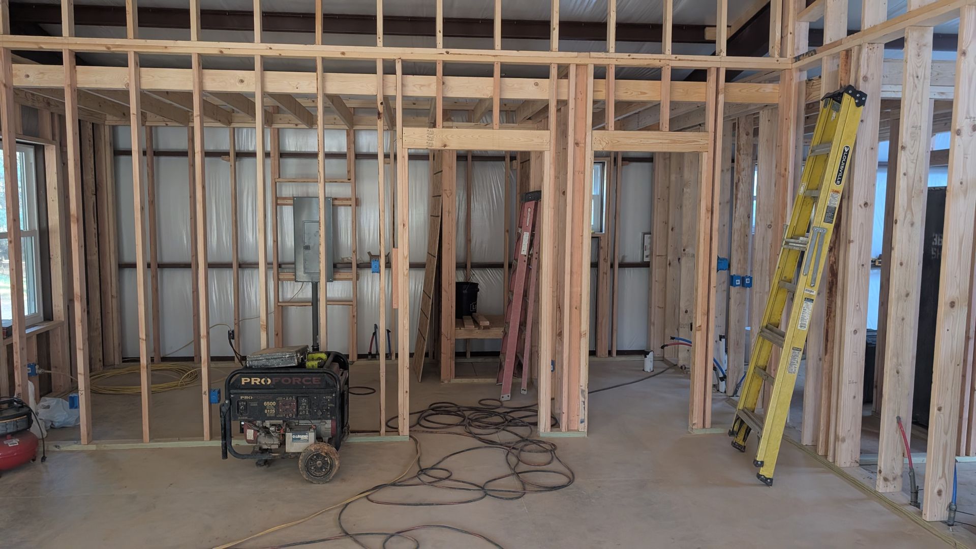 Interior of a building under construction, framed walls, generator, ladder, and wires.