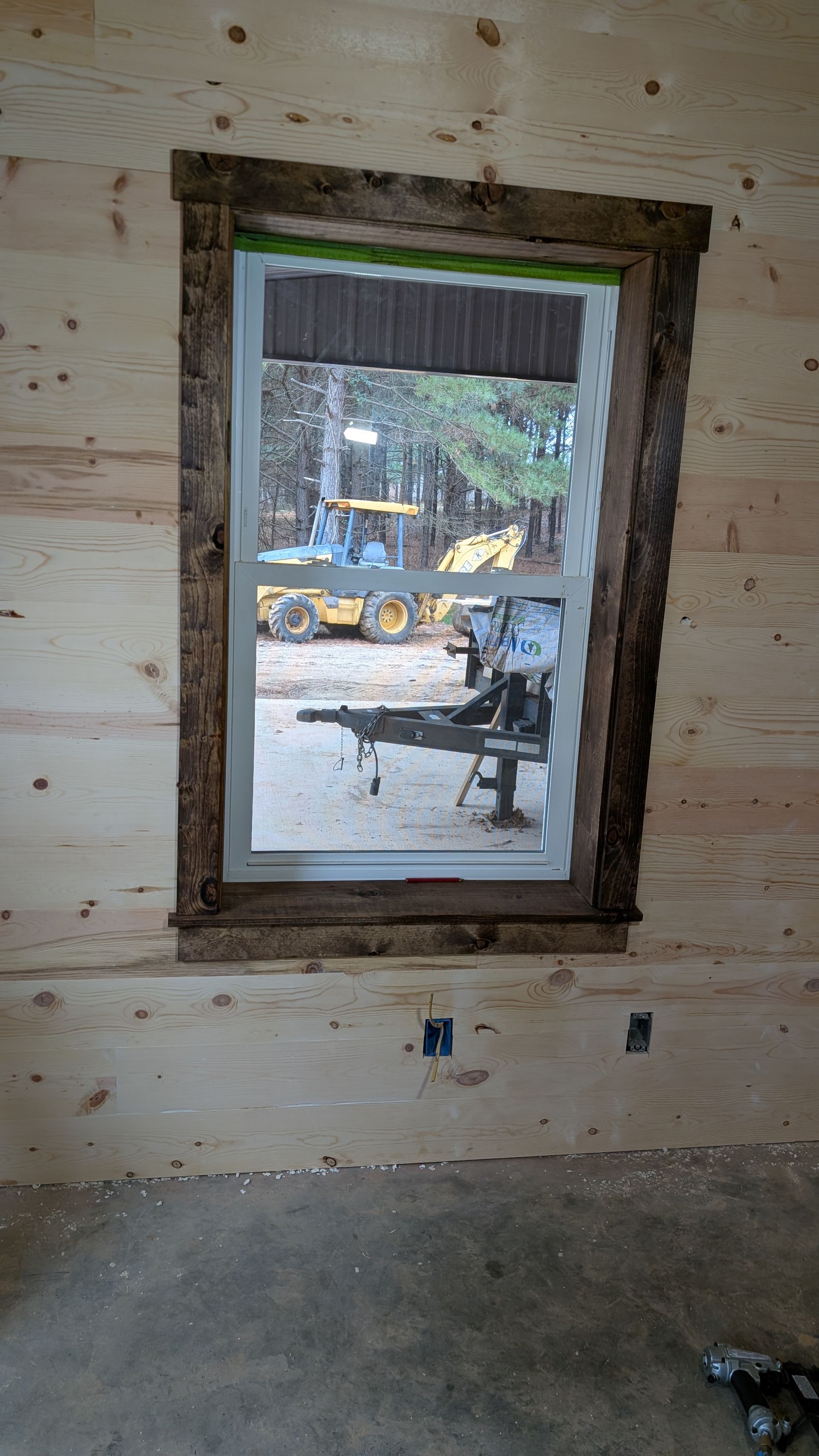 Window with rough-hewn wooden trim set in a cabin wall, view of outdoor construction equipment.