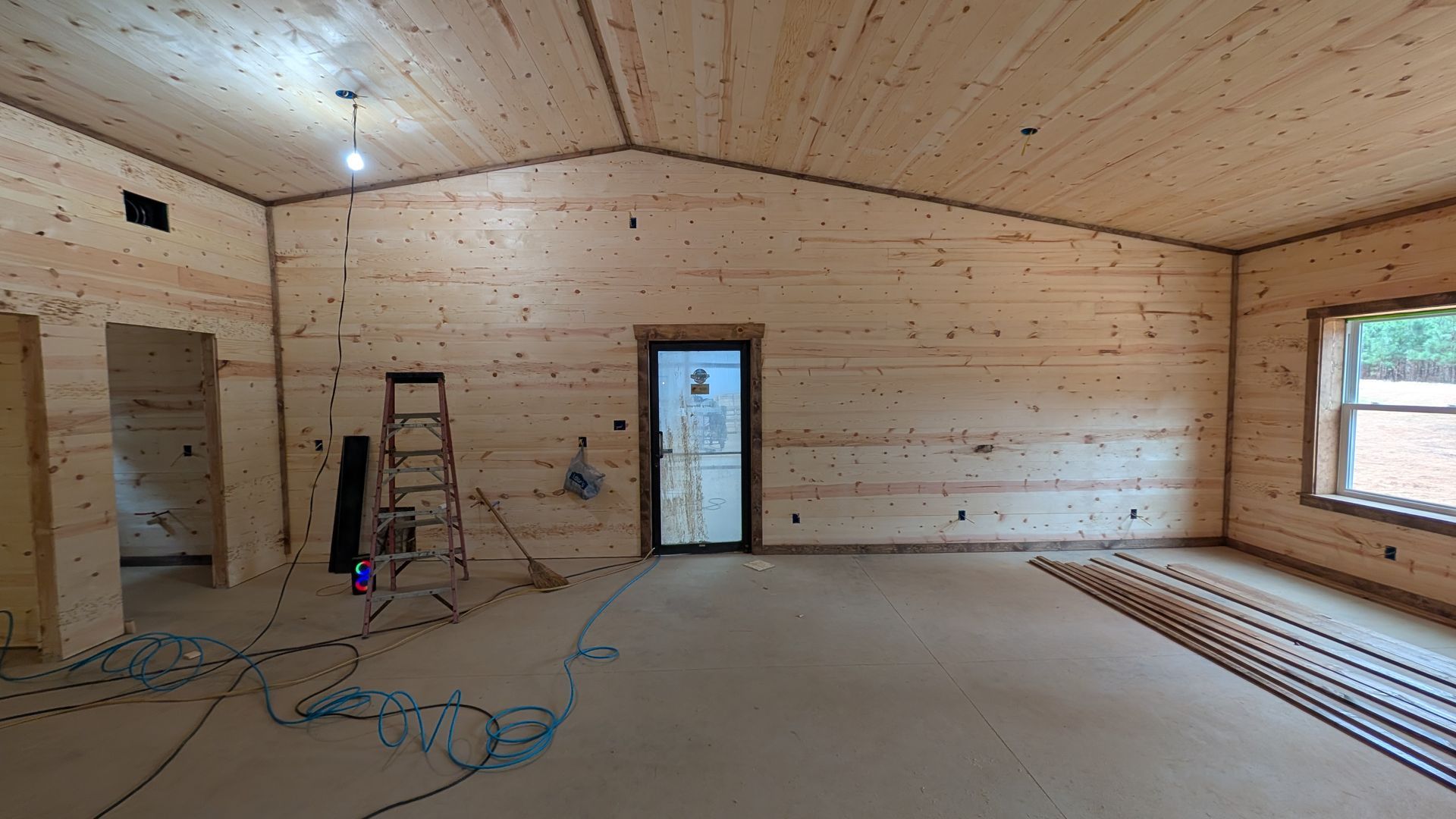 Interior view of a building under construction, featuring wooden walls and ceiling, a door, a window, and wiring.