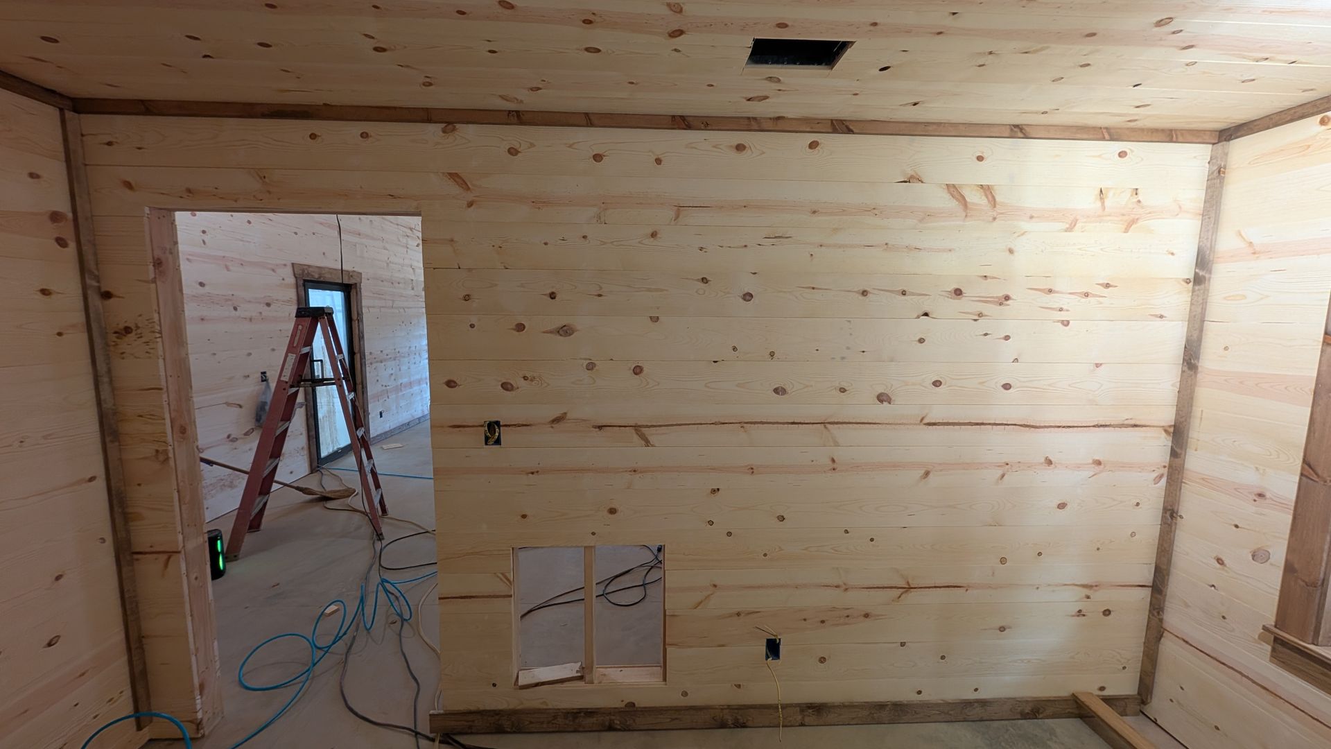 Interior room under construction, with wood panel walls and doorway to another room.
