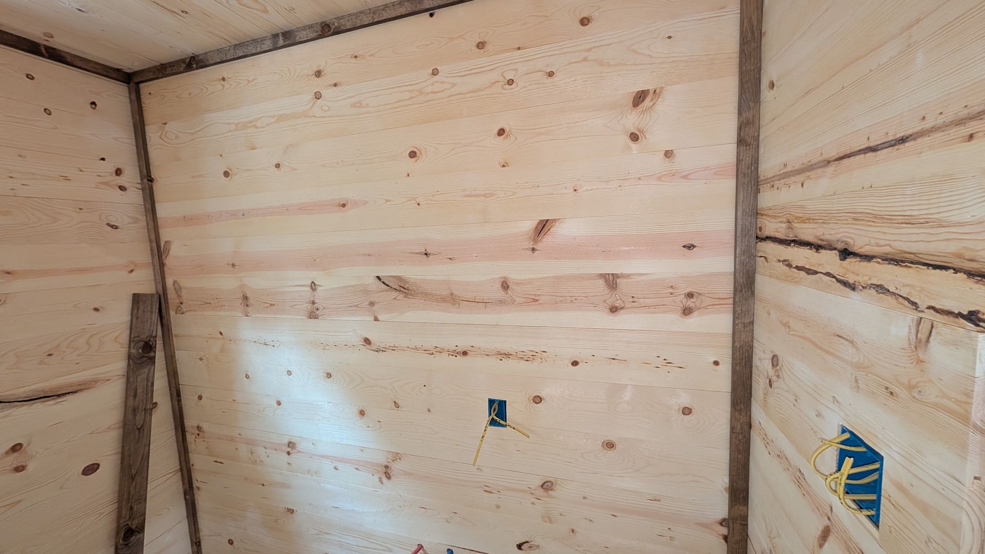 Interior of a room with unfinished wooden walls and a black electrical outlet.