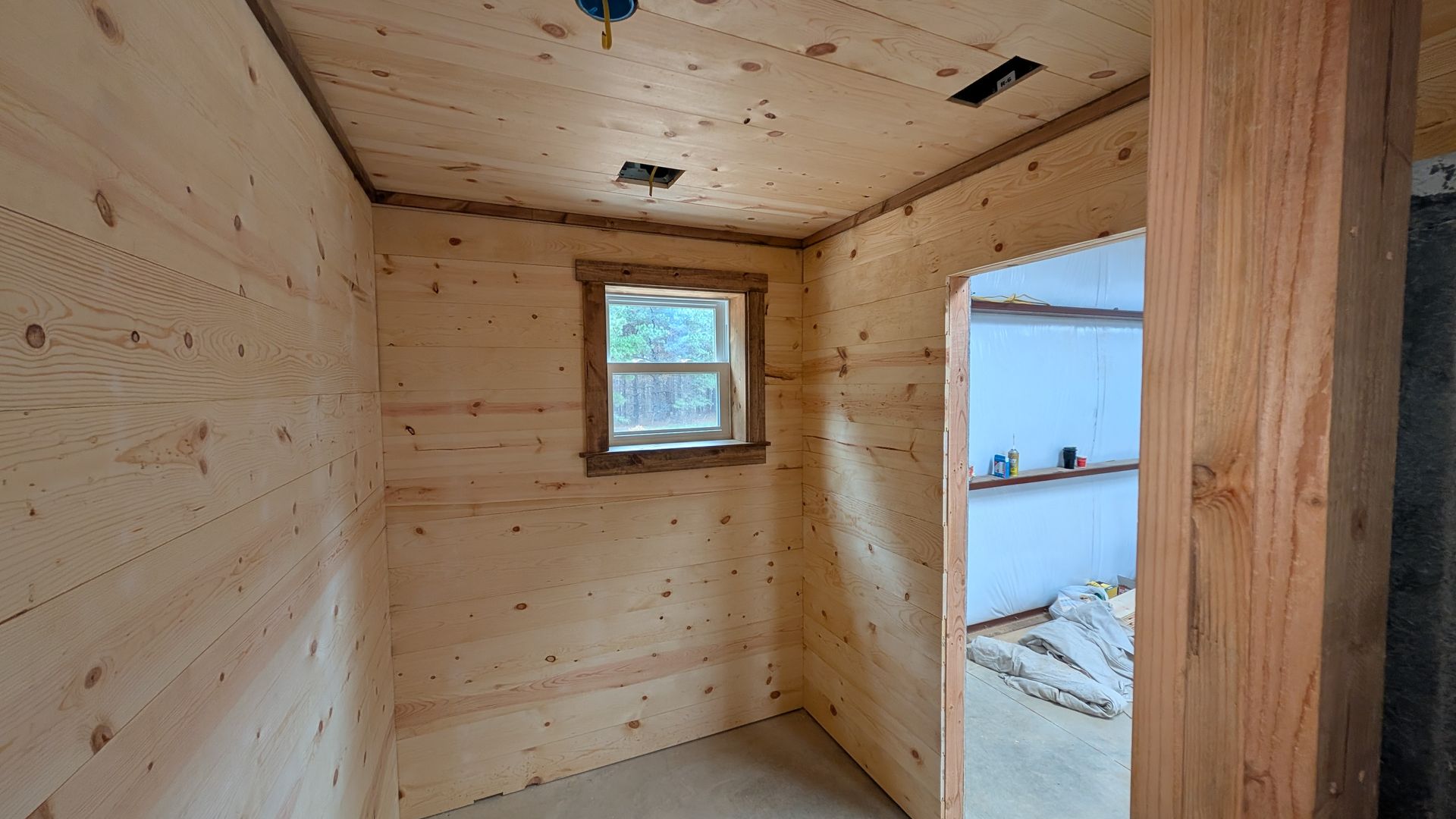 Interior view of small room with wooden walls and ceiling, window. Doorway visible.
