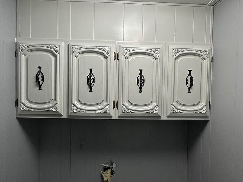 A laundry room with white cabinets and black handles