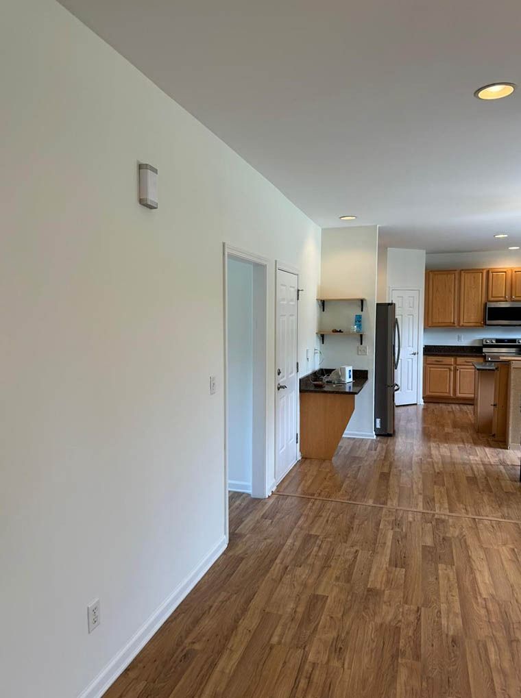 A hallway leading to a kitchen with hardwood floors and white walls.