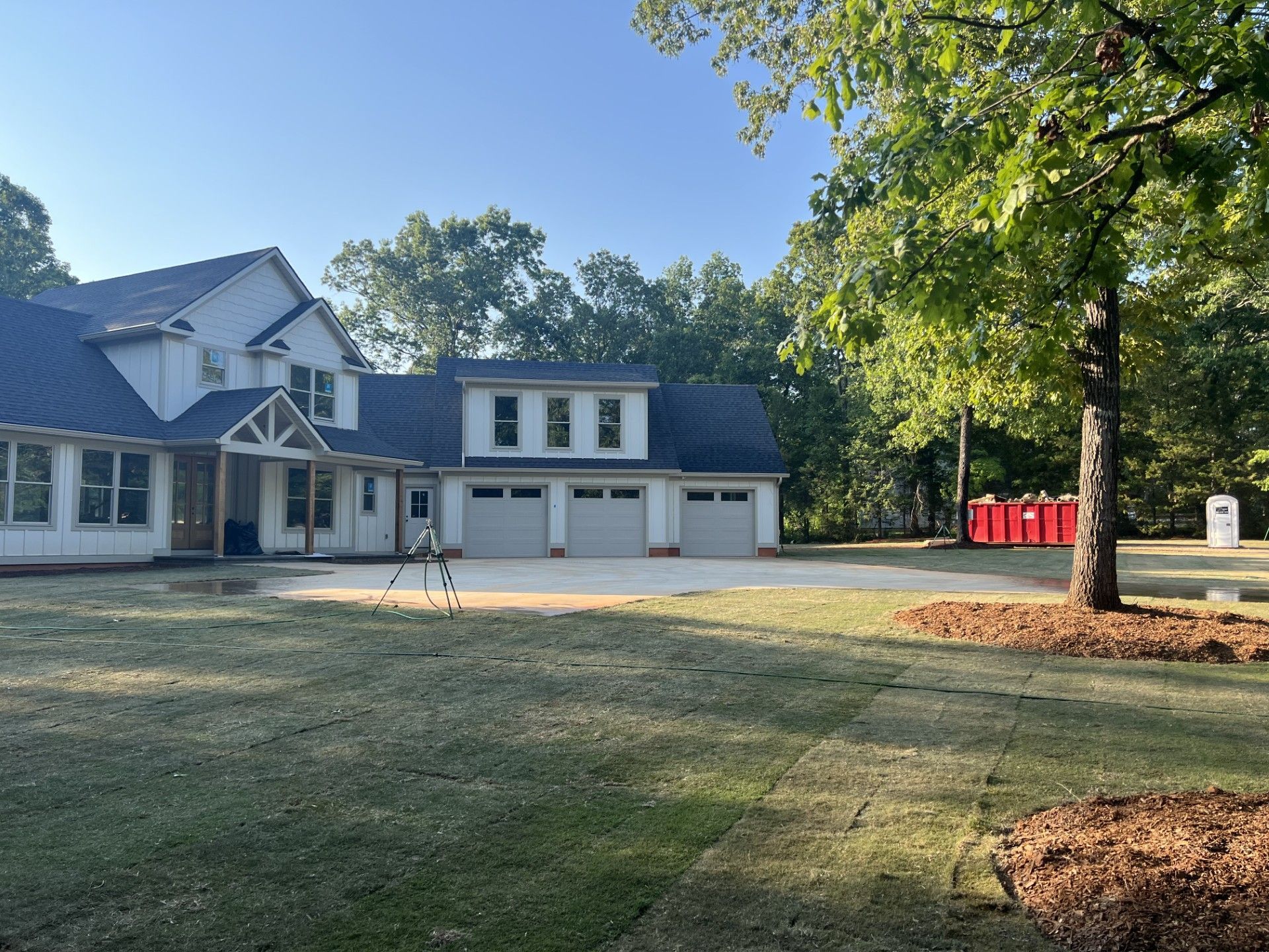 Large two-story house with three-car garage, construction materials, and portable toilets in the yard.