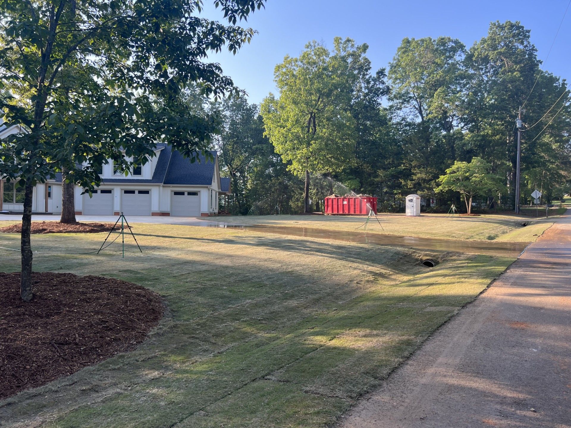 Newly sodded lawn next to a road, with a house in the background and construction materials in the middle.