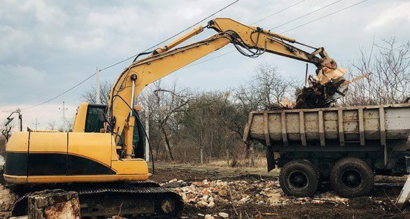 An excavator loading dirt into a dump truck | Land Clearing