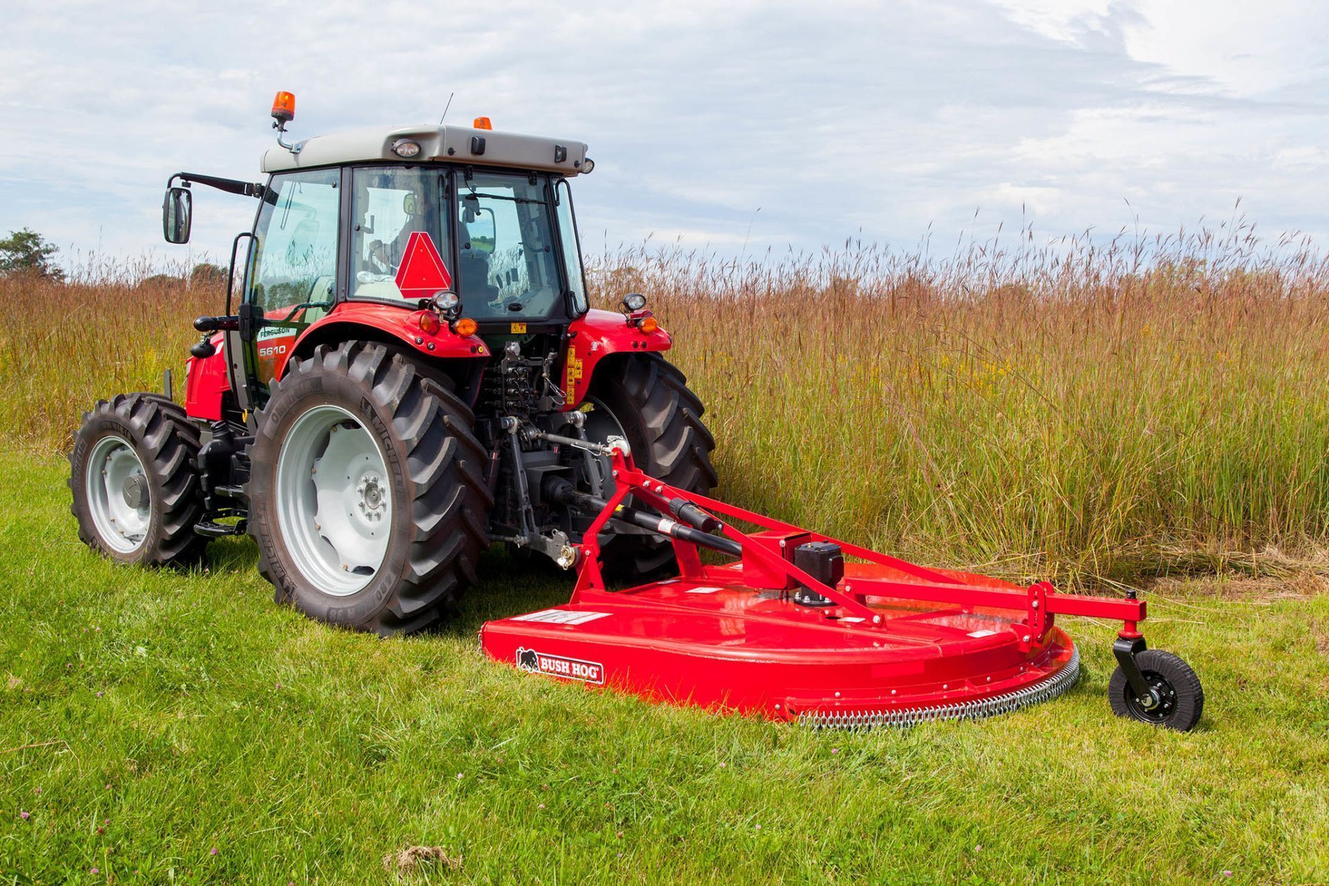 A red tractor is cutting grass in a field.