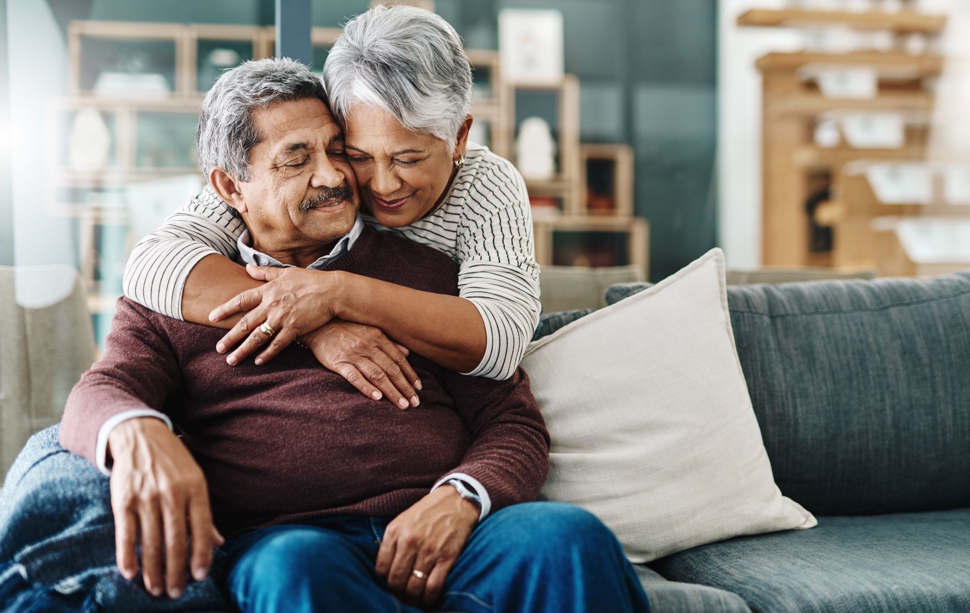 An elderly couple is sitting on a couch hugging each other.