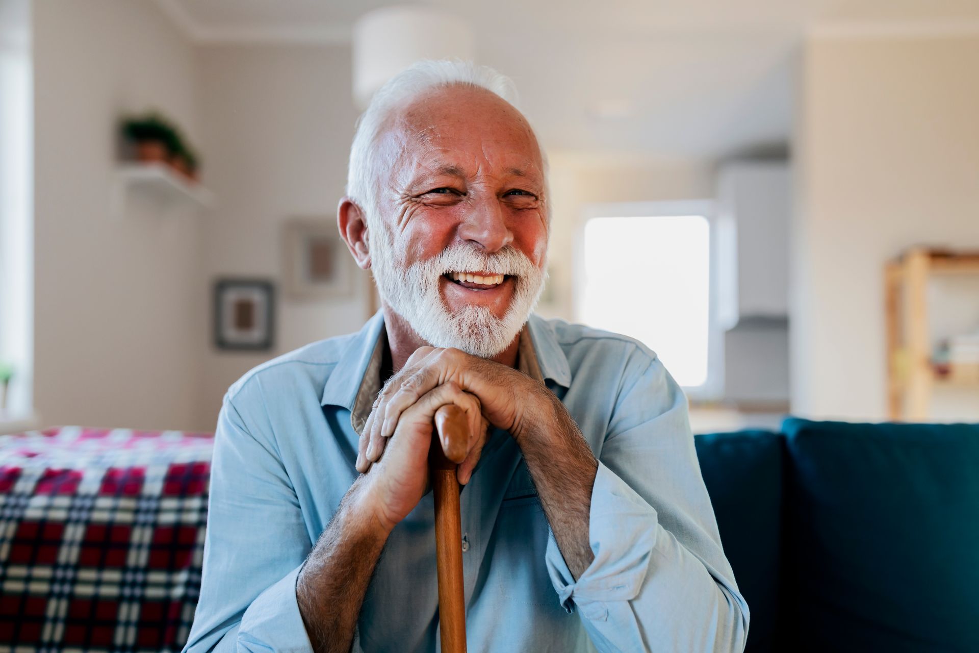 An elderly man is sitting on a couch with a cane and smiling.