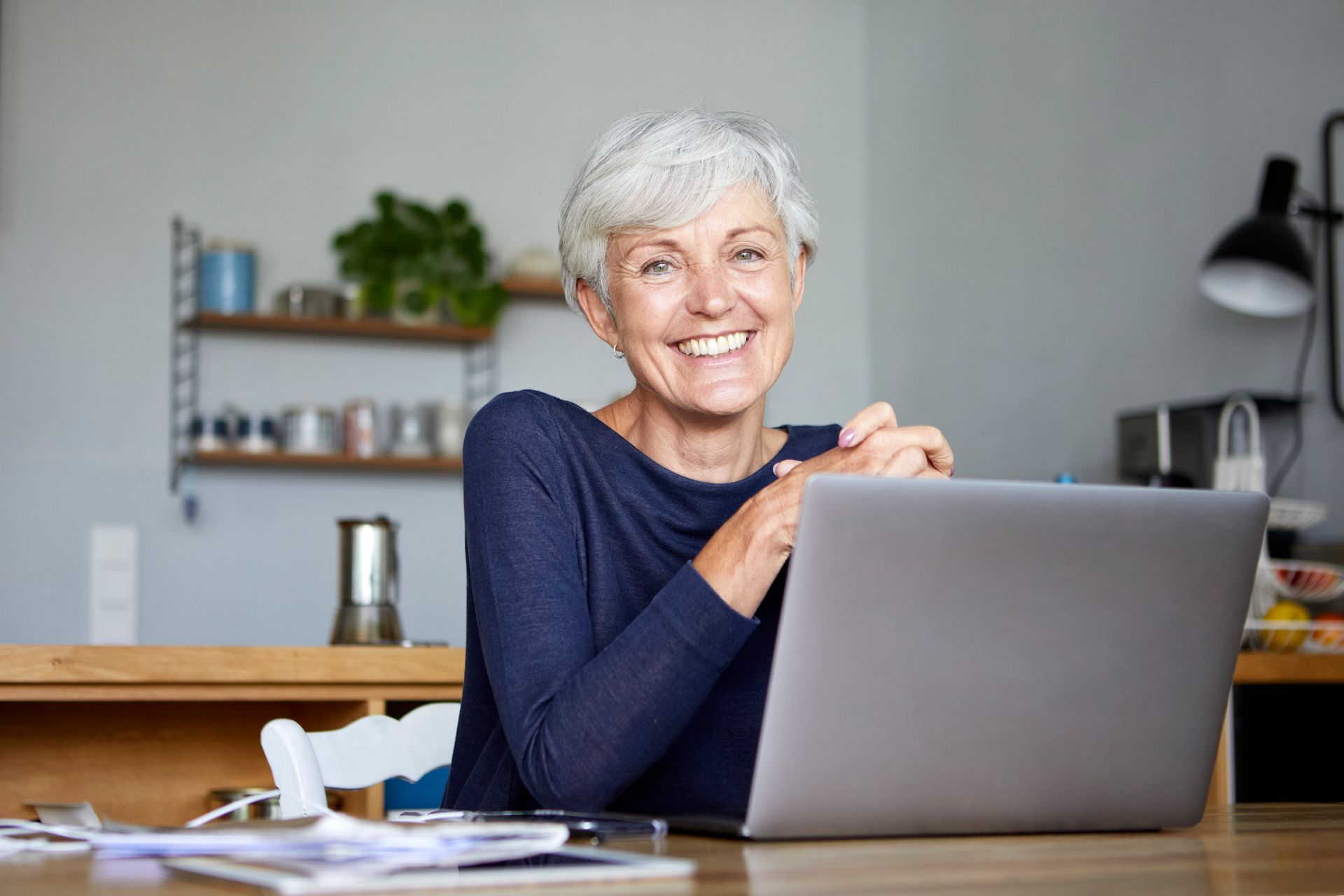 An older woman is sitting at a desk using a laptop computer.
