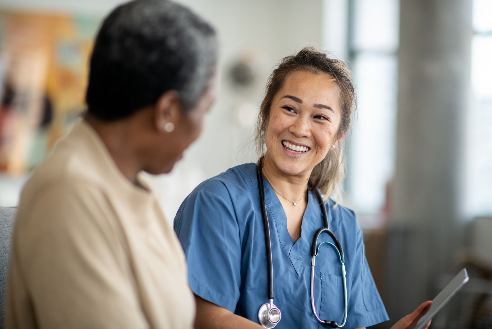 A nurse is talking to an elderly woman while holding a tablet.