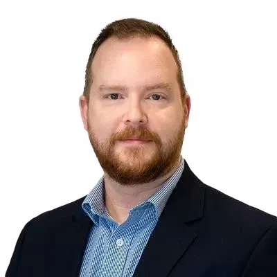 A man with a beard is wearing a suit and a blue shirt.