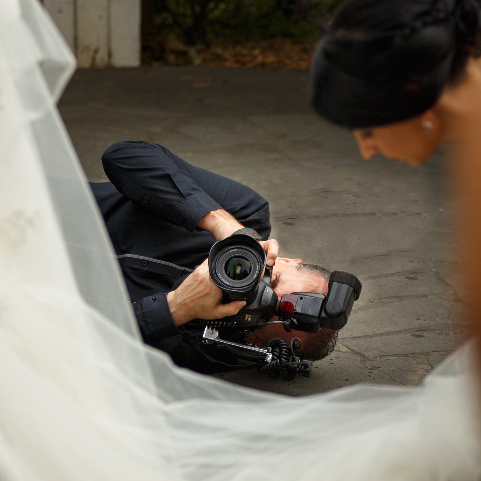 A man is laying on the ground taking a picture of a bride