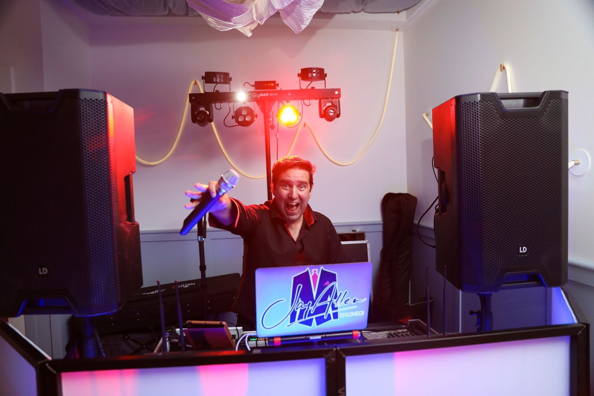 Jay Allen wedding DJ and MC is standing behind a dj booth holding a microphone.
