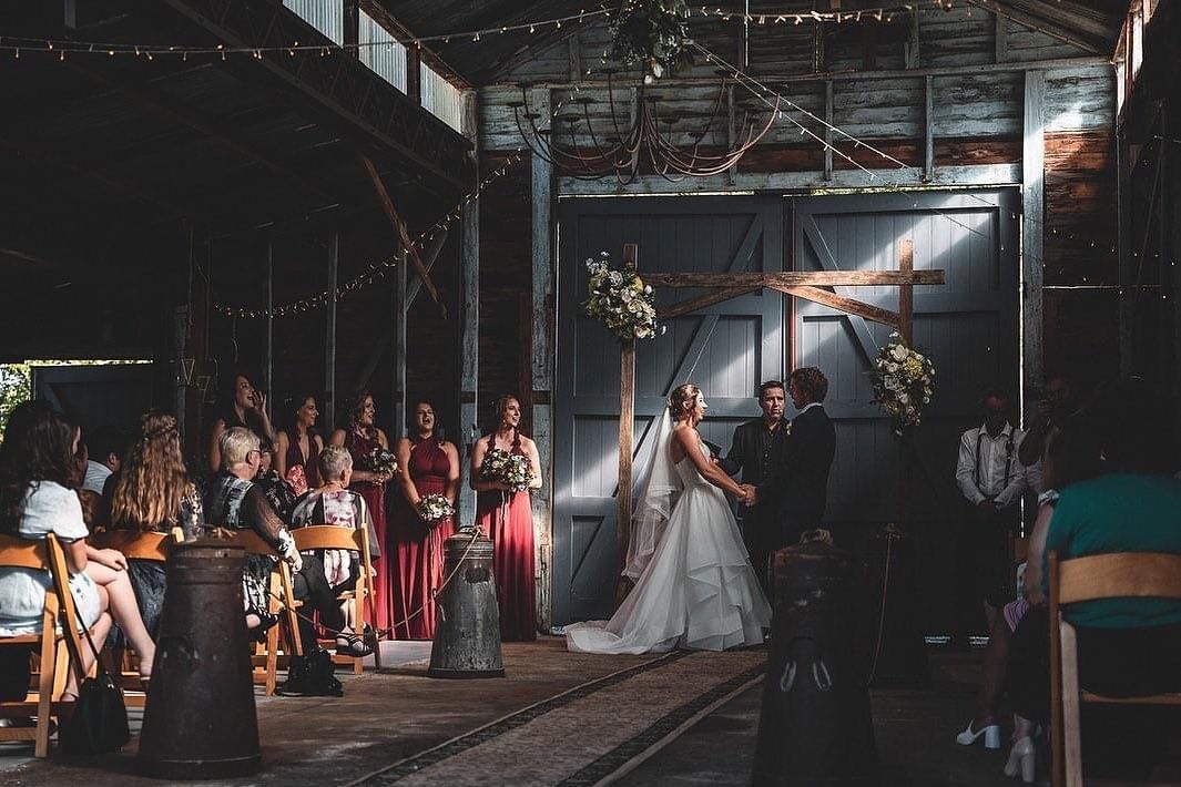 A bride and groom are holding hands during their wedding ceremony in a barn.