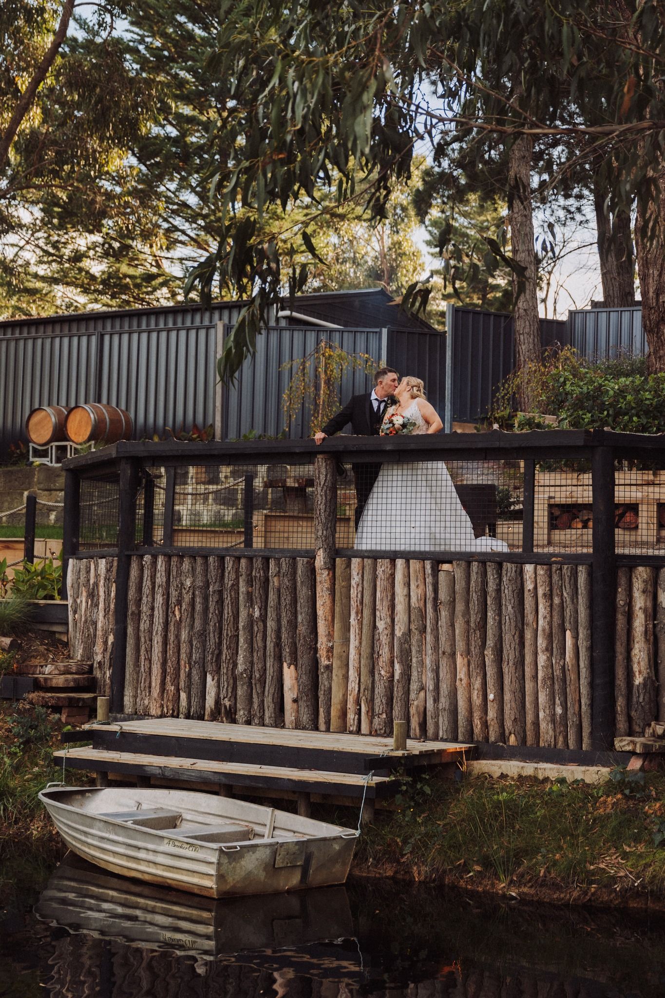 A bride and groom are kissing on a wooden bridge over a river.