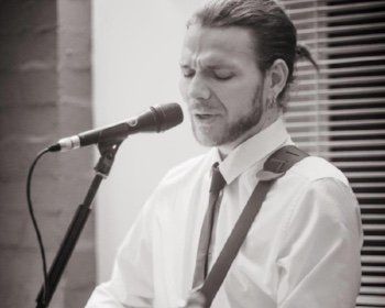 A man in a white shirt and tie is singing into a microphone.