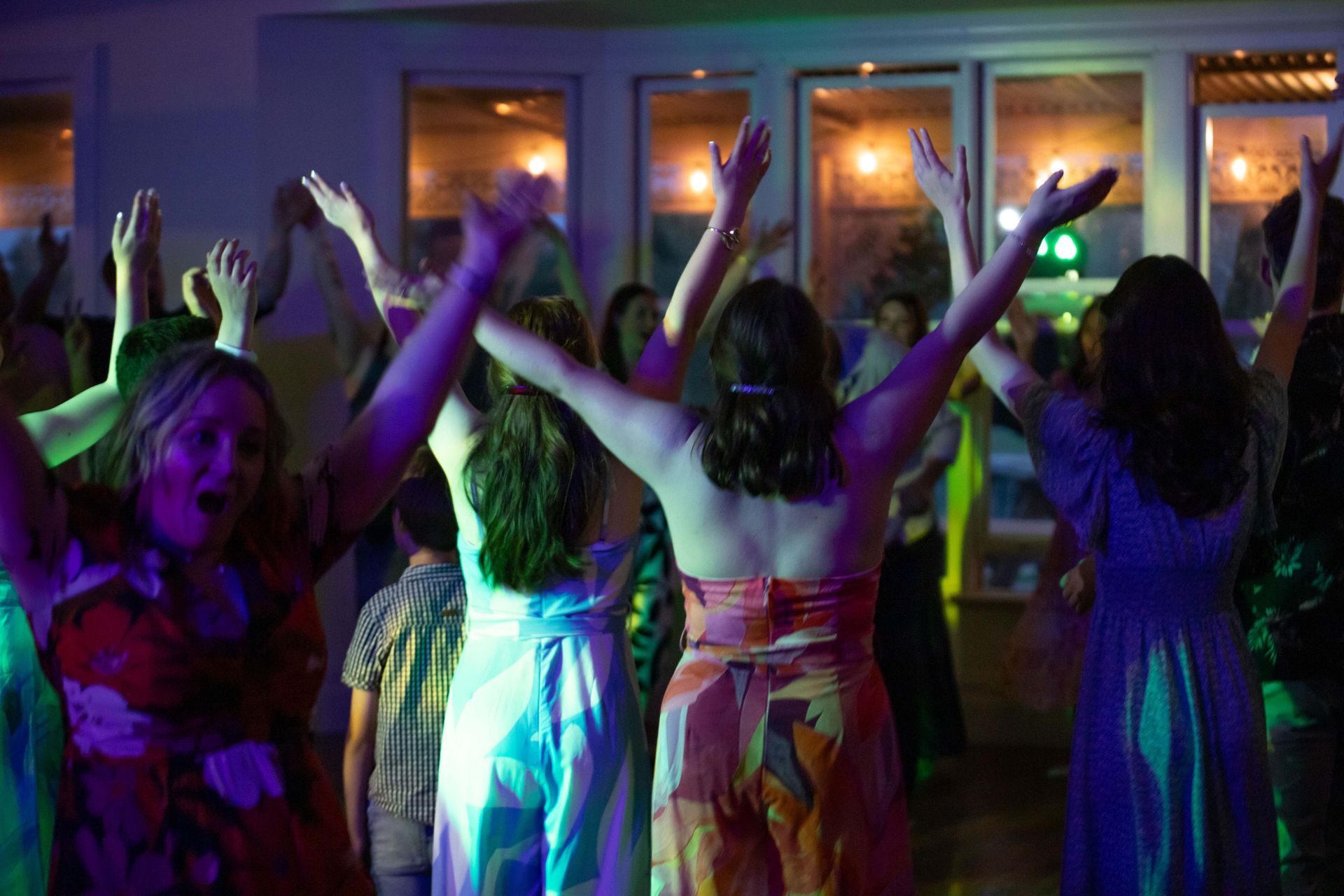 People dancing with arms raised in a brightly lit room.