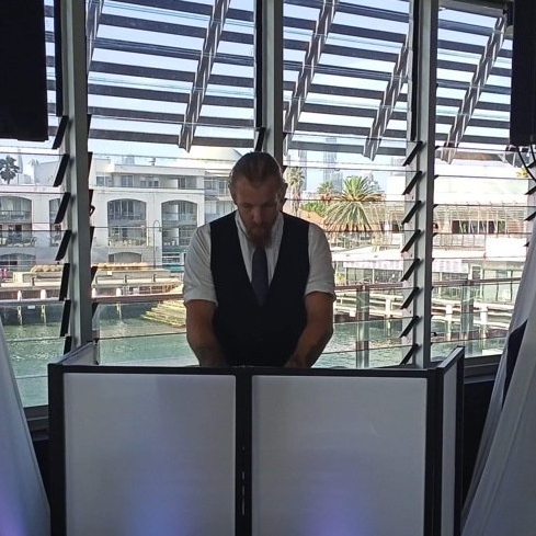 A man in a suit and tie is standing in front of a dj booth.