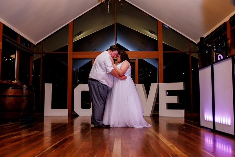 A bride and groom are dancing in front of a large love sign.