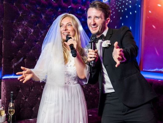 A bride and groom are singing into microphones at their wedding reception.