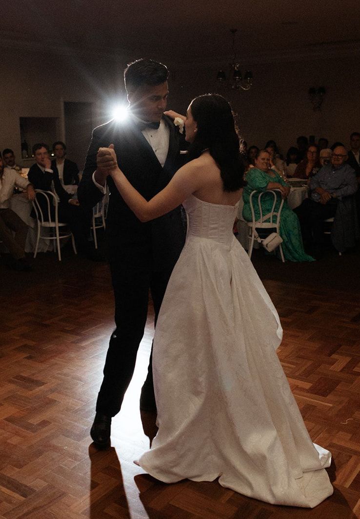 A bride and groom are dancing in front of a crowd at their wedding reception.
