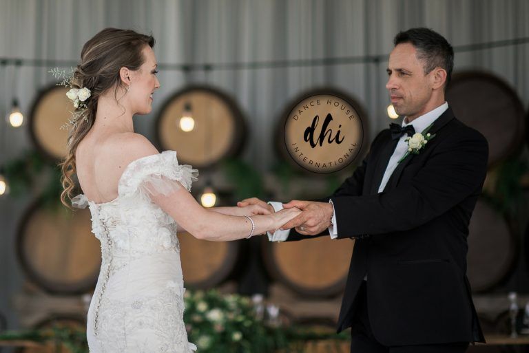 A bride and groom are holding hands in front of wine barrels.