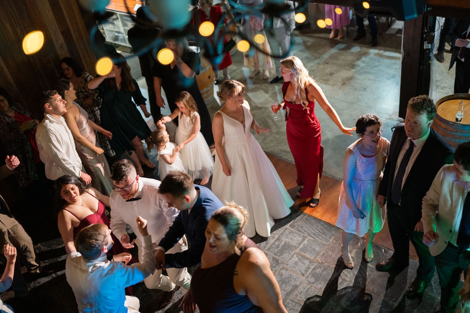 Wedding reception with dancing guests under warm lights. Bride in white gown, a woman in a red dress.