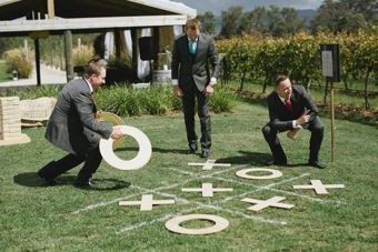 Three men in suits are playing a game of tic tac toe on the grass.