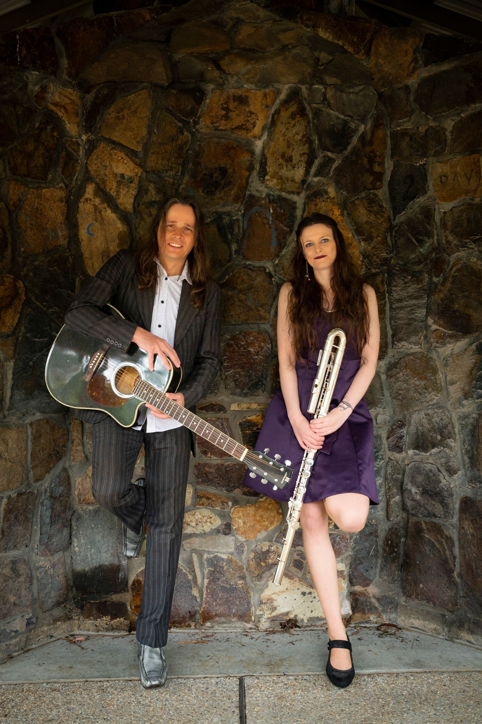 A man is holding a guitar and a woman is holding a flute.