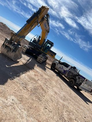 A truck is parked next to an excavator on a dirt road.