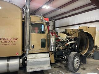 A semi truck is sitting in a garage with its hood open.