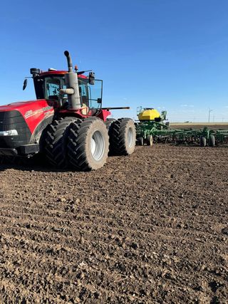 A red tractor is plowing a field next to a green tractor.