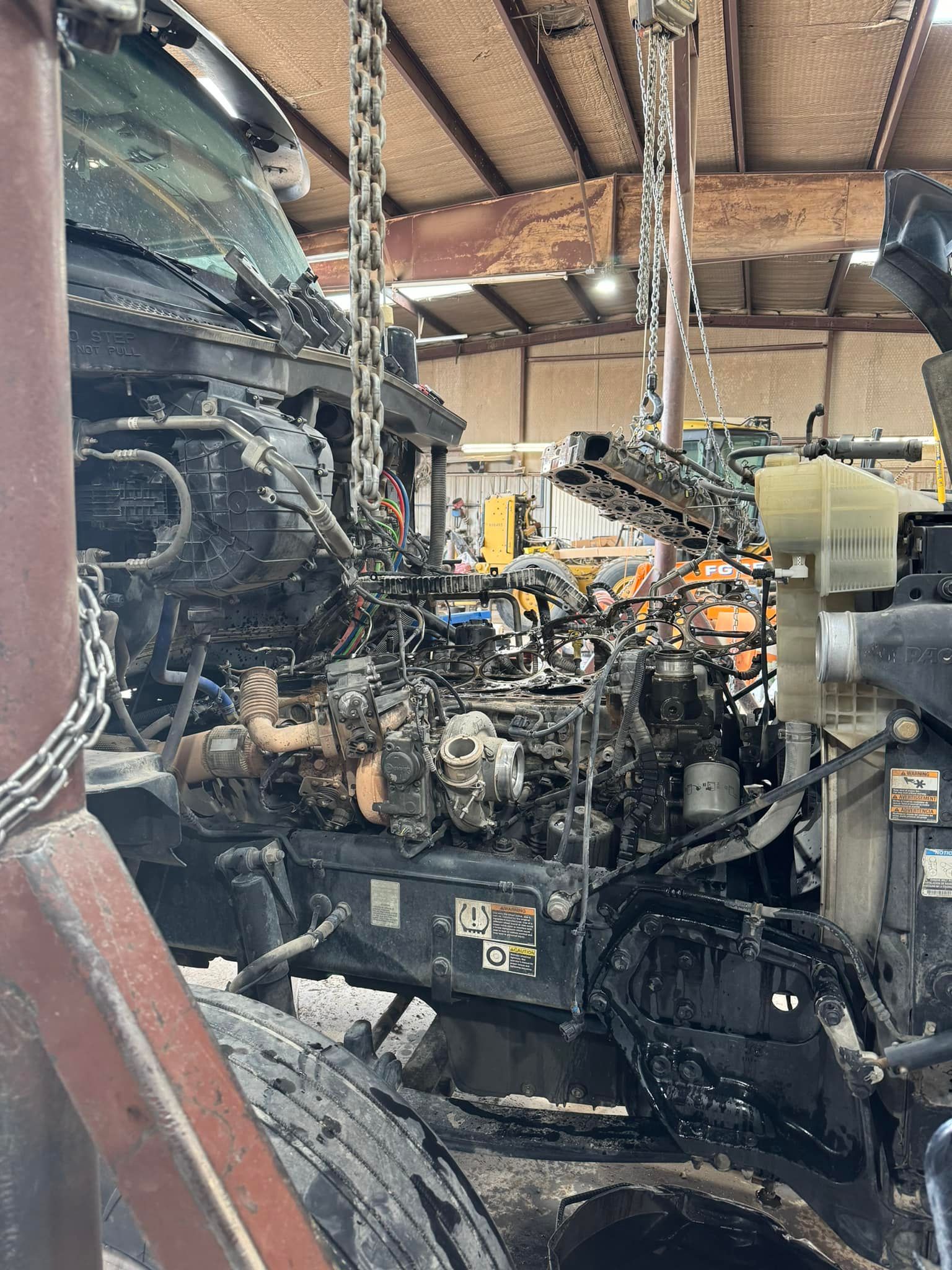 A truck engine is being removed from a truck in a garage.