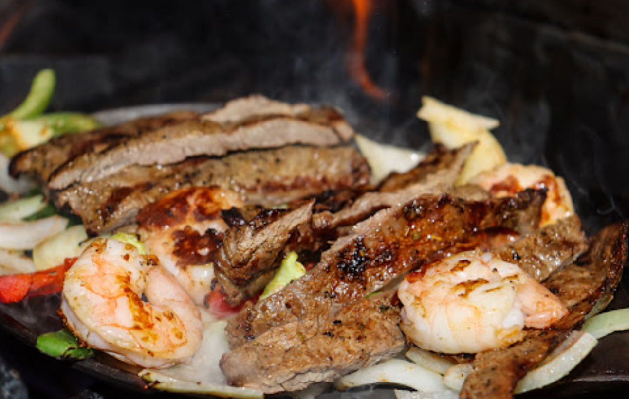 A close up of a plate of food with meat and shrimp on a grill.