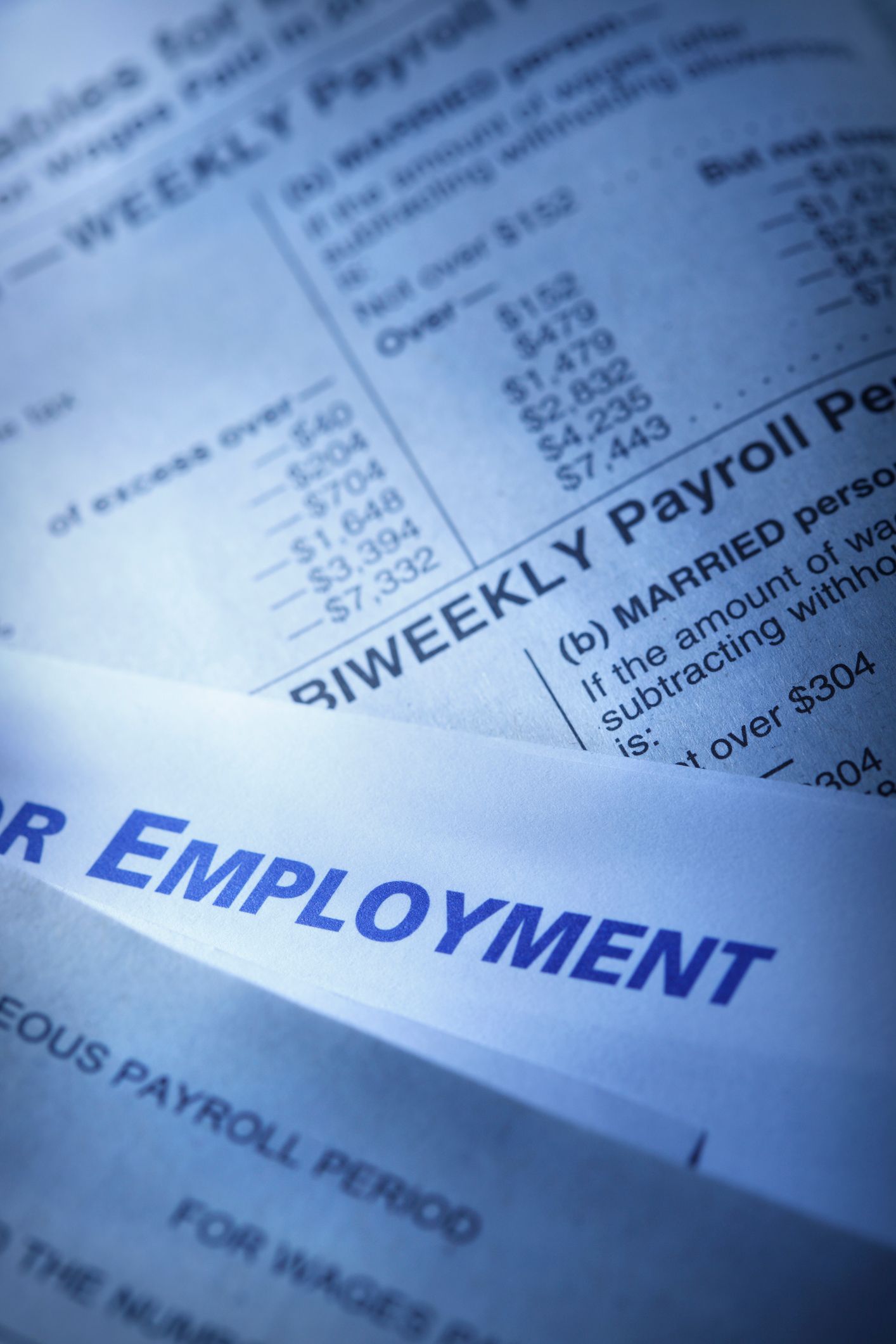 Close-up of blue-tinted employment and payroll documents with financial data and tables.