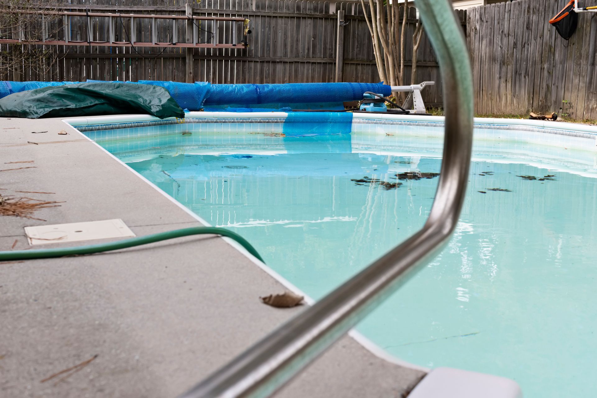 Backyard pool with debris on water surface prepared for swimming pool closing services.