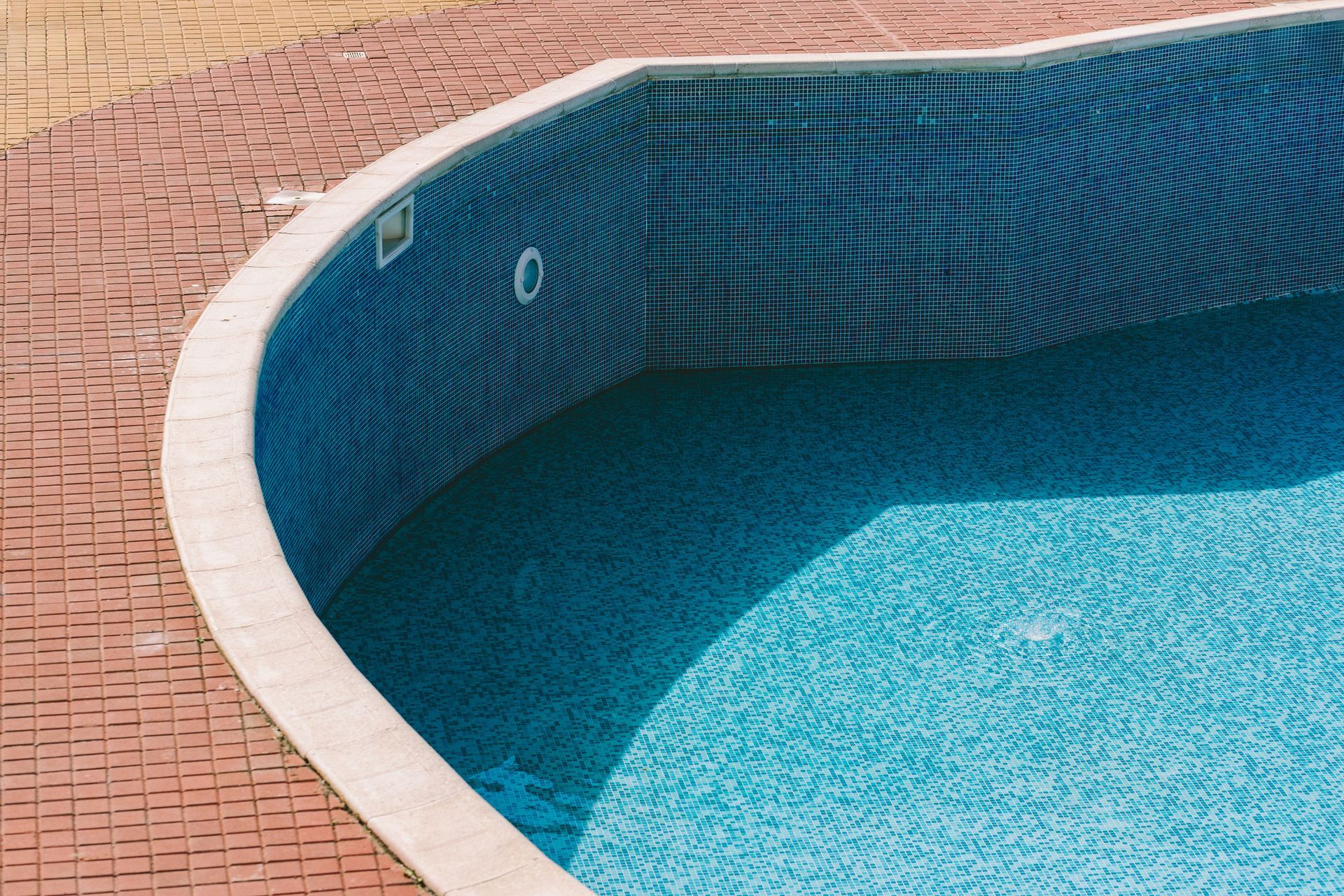 Empty swimming pool with blue mosaic tiles and red brick deck. Empty swimming pool with blue mosaic tiles and red brick deck.