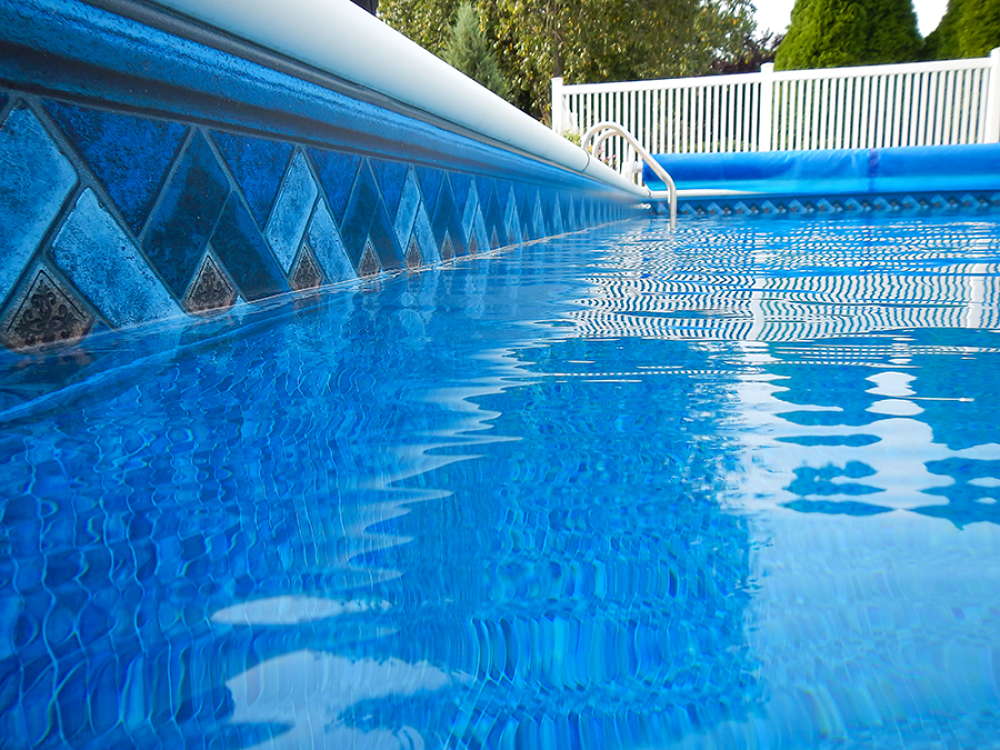 Blue tiled swimming pool with rippled water, white fence in the background.