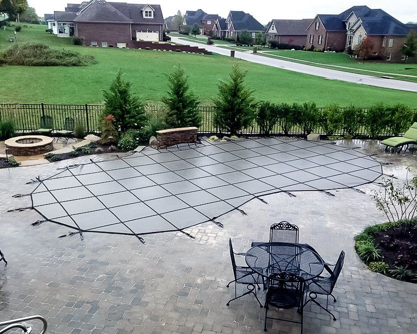 Patio with pool cover, fire pit, and outdoor furniture in a suburban backyard.