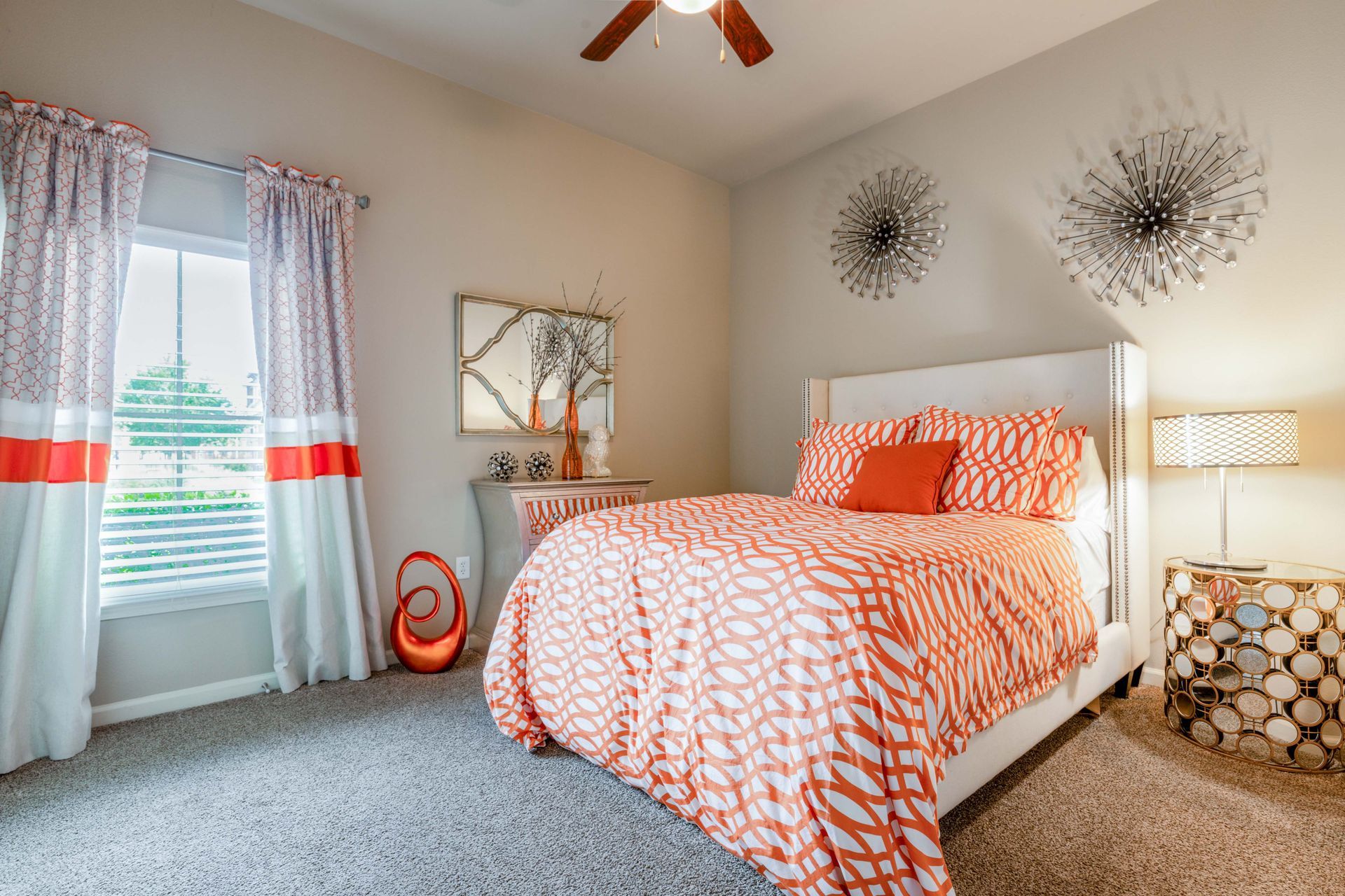 Bedroom with orange patterned bedding, curtains, and decor. Gray walls and carpet.
