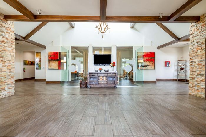Lobby with wood beams, TV over a console, wood-look flooring, glass walls, and artwork.