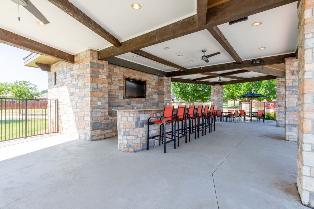 Outdoor bar area with stone walls, a long bar with red bar stools, and a TV.