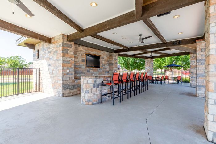 Outdoor bar area with stone walls, a long bar with red bar stools, and a TV.