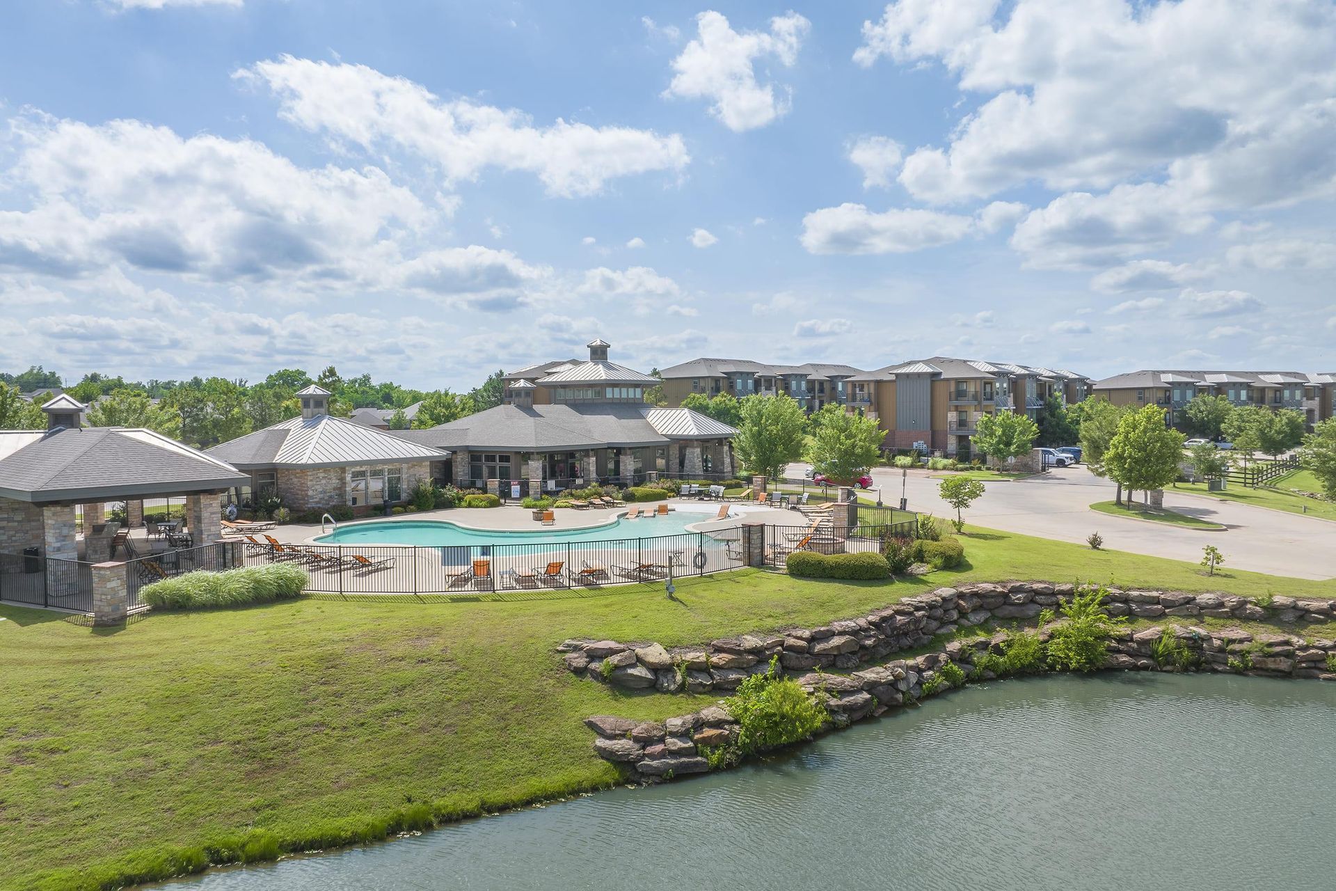 Lakeside apartment complex with a pool, gazebo, and several buildings under a cloudy sky.