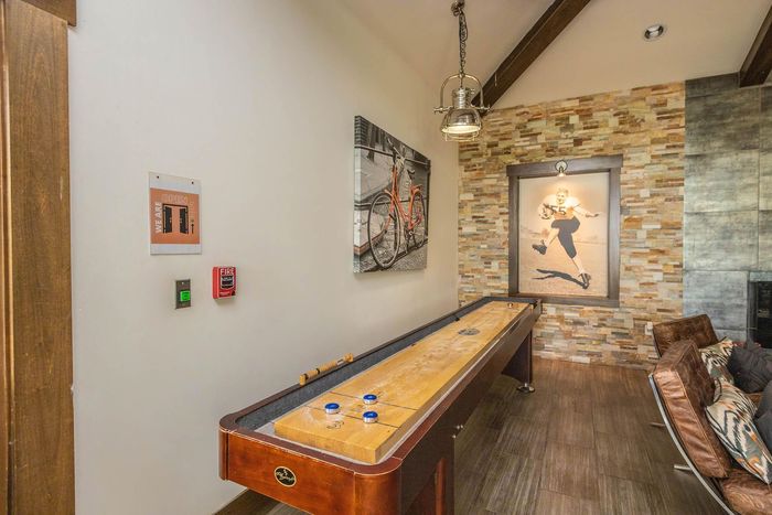 Shuffleboard table in a rustic room with artwork, exposed stone, and a hanging light.